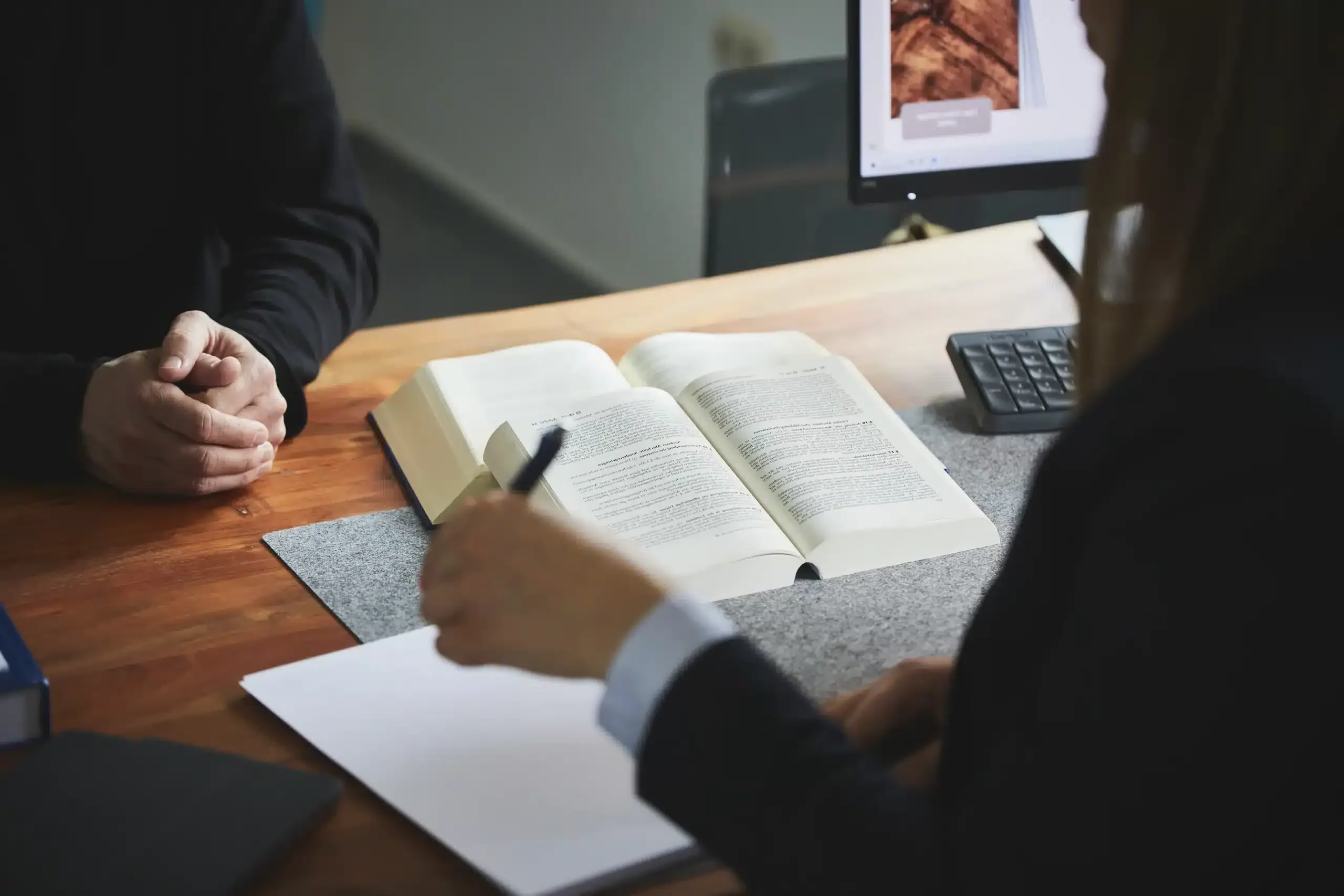 Anwalt und Mandant bei der Besprechung eines Aufhebungsvertrags mit einem offenen Gesetzbuch auf dem Tisch.